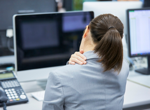 Mulher no ambiente de escritório segurando o pescoço, demonstrando dor e desconforto por fibromialgia durante o trabalho.