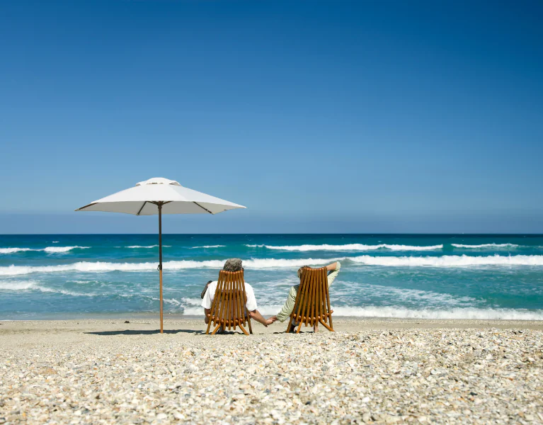 Casal aposentado relaxando na praia após um planejamento previdenciário bem feito